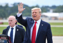 Donald Trump waves while walking outdoors with security nearby