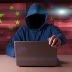 Hooded figure using a laptop with red cybersecurity graphics