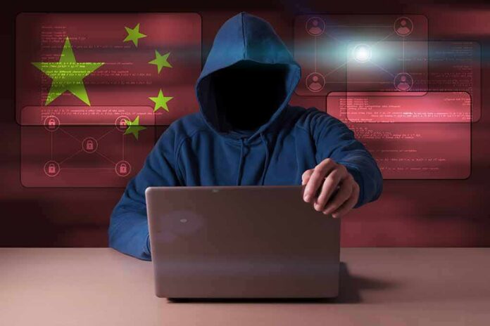 Hooded figure using a laptop with red cybersecurity graphics