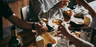 Hands toasting wine glasses over a cheese board