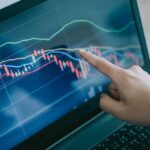 Hand pointing at stock chart on laptop screen