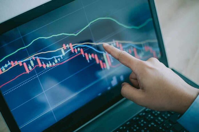Hand pointing at stock chart on laptop screen