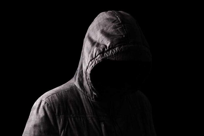 shutterstock_1185428734 Hooded figure in shadow on black background