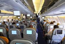 Interior view of an airplane with passengers seated and using in-flight entertainment screens
