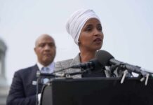 1 Missing Record Could Unravel Ilhan Omar’s CITIZENSHIP Ilhan Omar speaking at a podium with André Carson standing behind