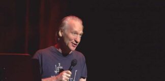 Bill Maher performing stand-up with a microphone on stage